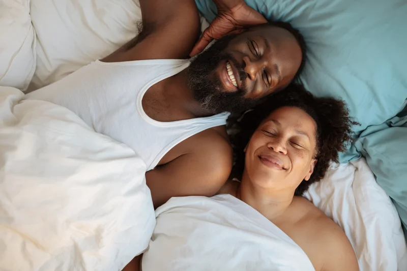 Smiling black couple lying together in bed under white sheets