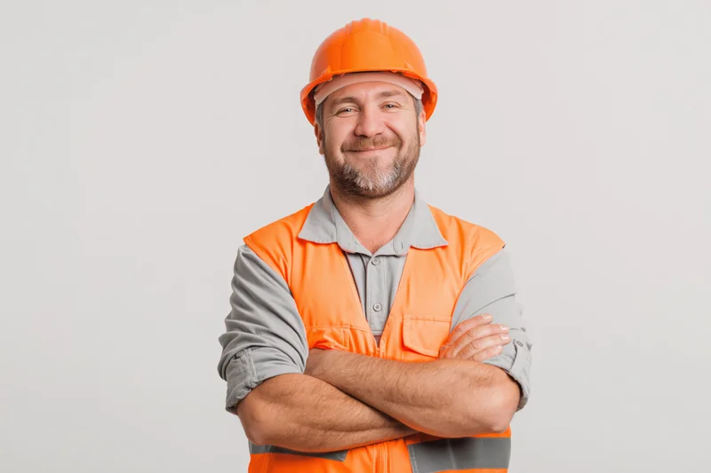 Smiling middle-aged man in orange safety helmet and vest with arms crossed against white background