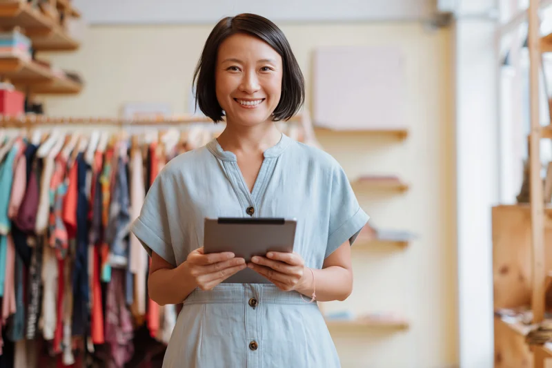 Smiling woman holding digital tablet in boutique clothing store
