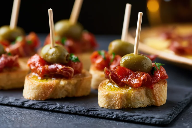 Spanish pintxos with jamon and olives on toasted bread served on a dark slate plate