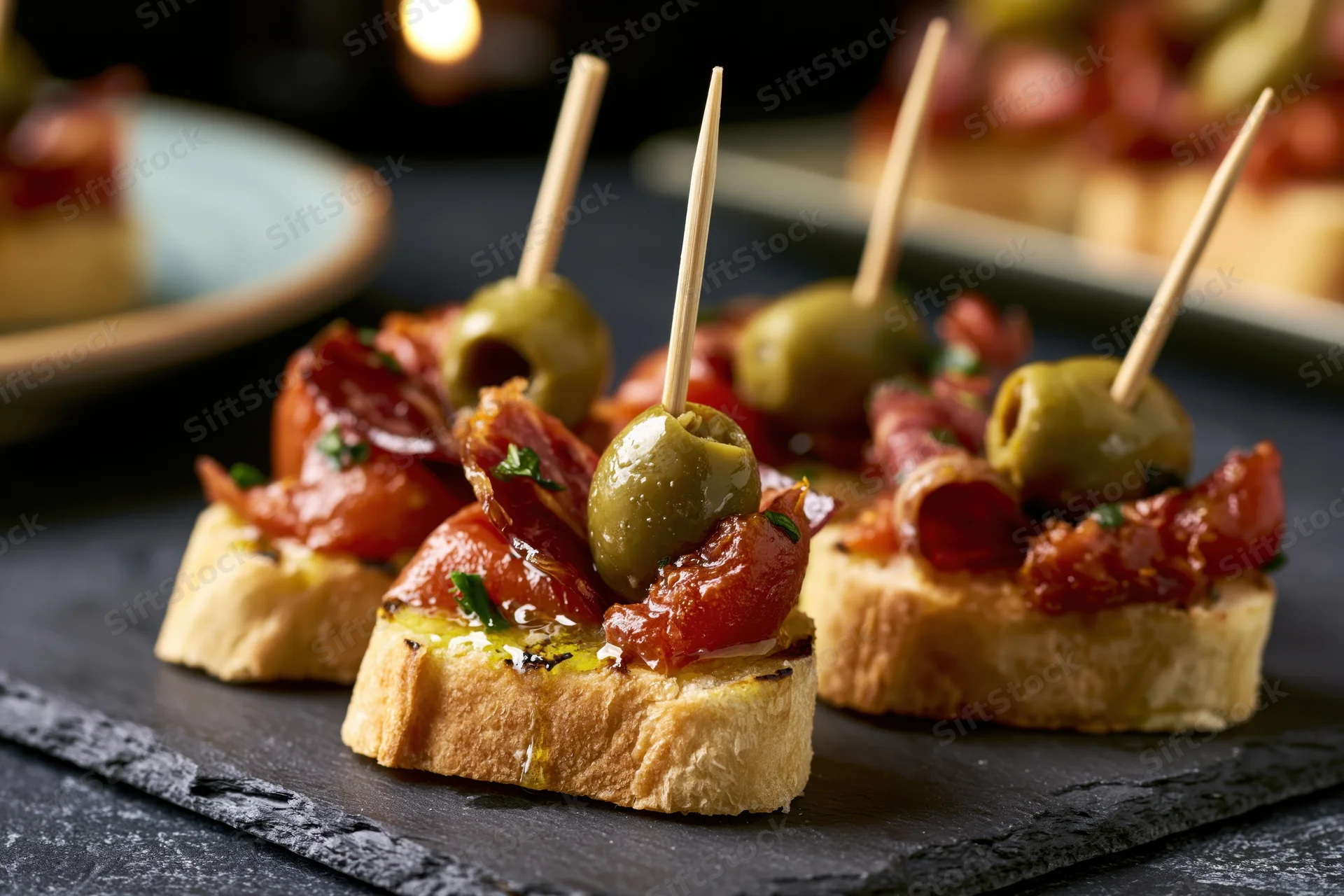 Spanish pintxos with olives and bacon on toasted baguette slices served on dark slate plate
