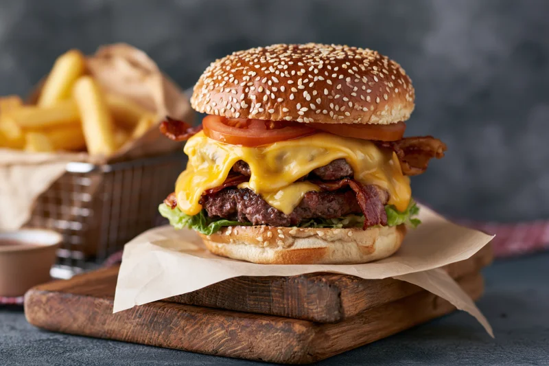 Double cheeseburger with bacon and melted cheese on sesame bun served with fries on wooden board