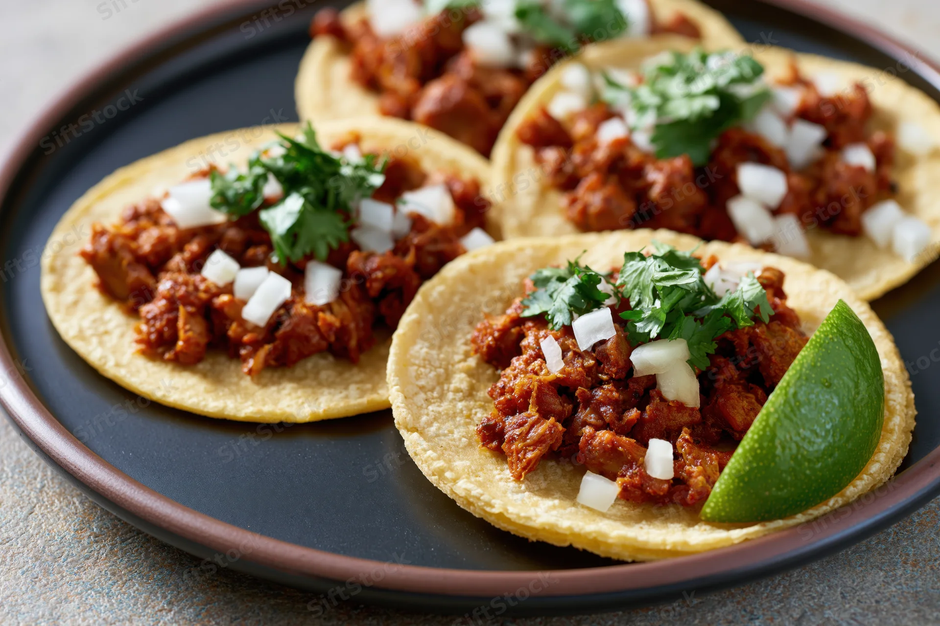 Al pastor tacos on small corn tortillas topped with diced onion, cilantro, and lime wedge on a black plate
