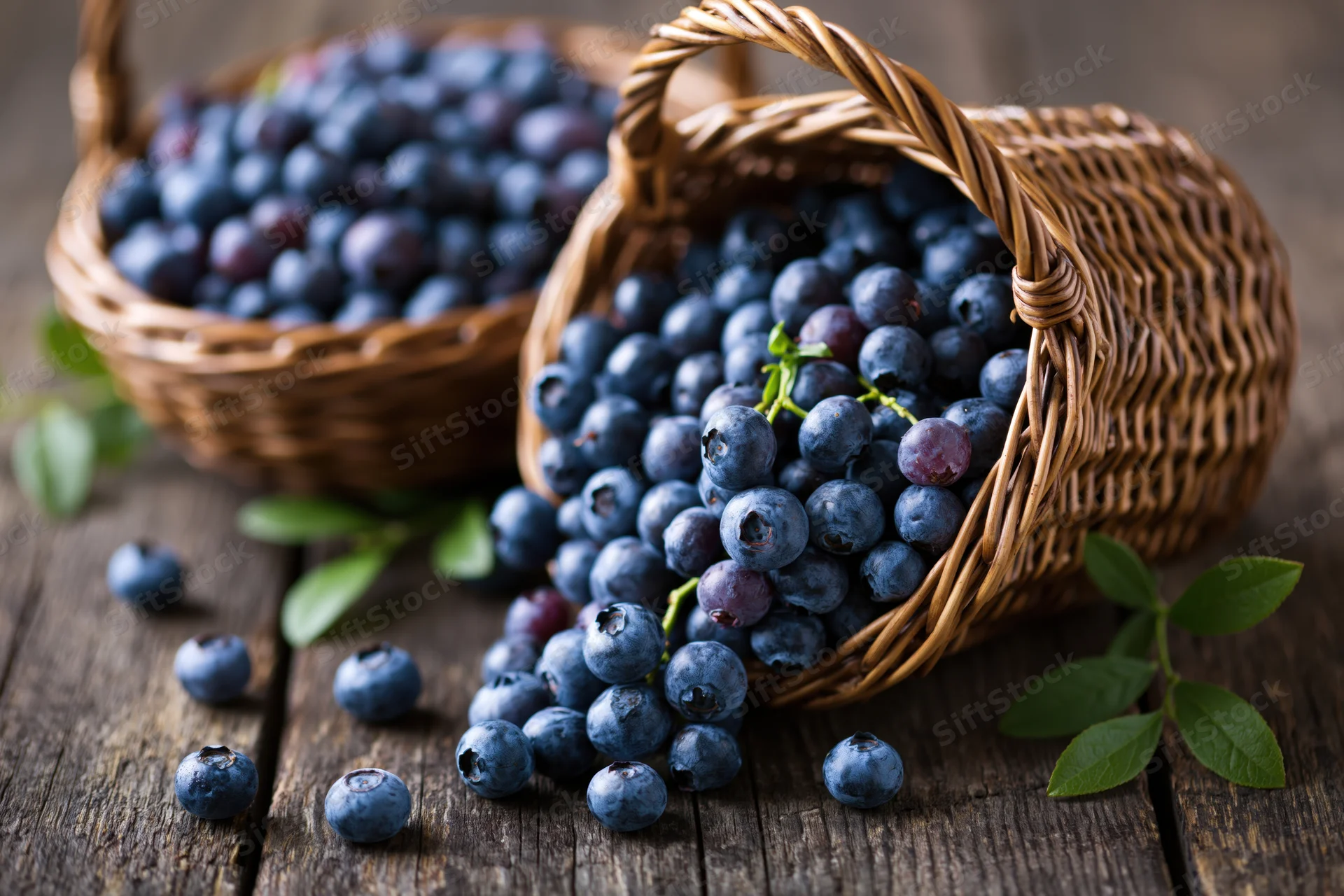 Fresh blueberries spilling from a wicker basket onto a wooden table with green leaves scattered around