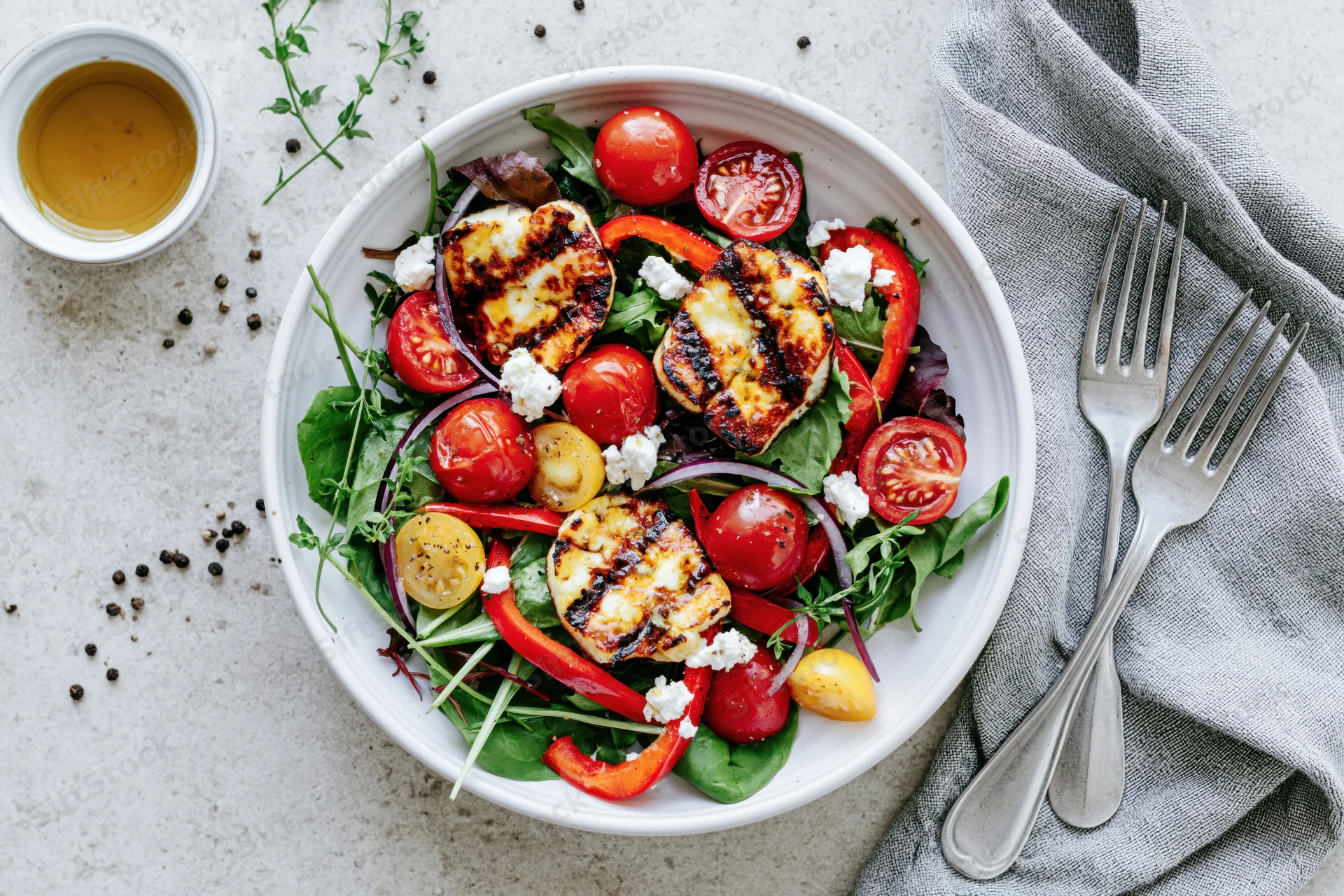 Grilled halloumi salad with cherry tomatoes and peppers in a white ceramic bowl on a kitchen countertop with forks and napkin