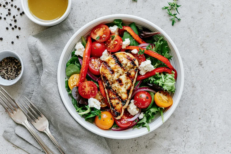 Grilled halloumi salad with cherry tomatoes and peppers in a white ceramic bowl on a countertop with cutlery and seasonings nearby