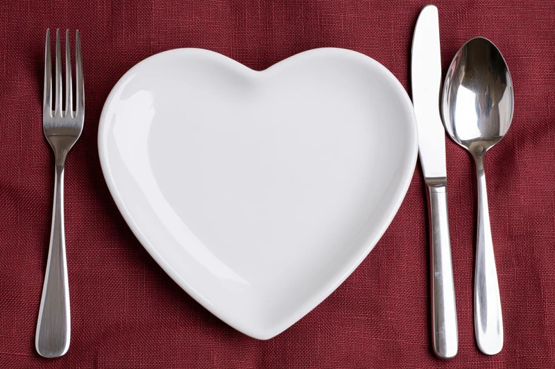 Heart-shaped white ceramic plate with silverware arranged on red linen tablecloth