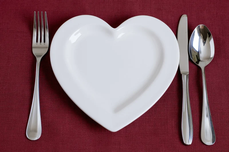 Heart-shaped white ceramic plate with silverware arranged on red linen tablecloth