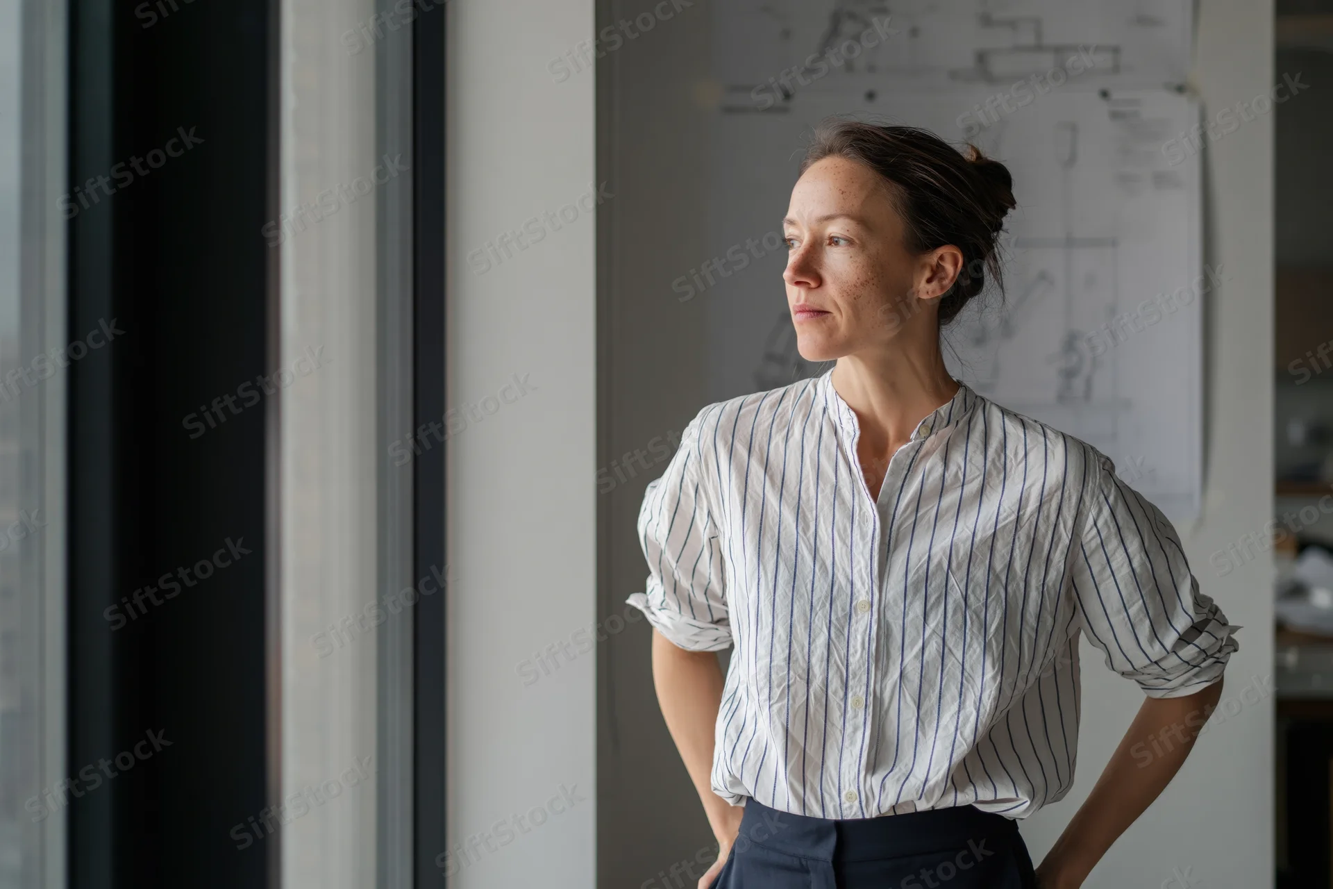 Woman architect standing by window looking thoughtful in office