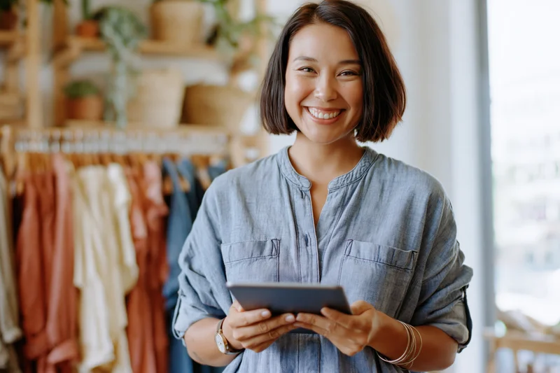 Woman smiling while holding tablet in boutique clothing shop