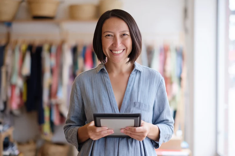 Woman smiling while holding tablet in boutique clothing store