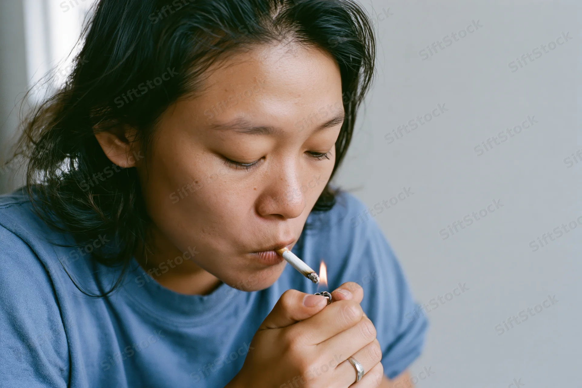Young asian woman lighting a cigarette held between her lips indoors