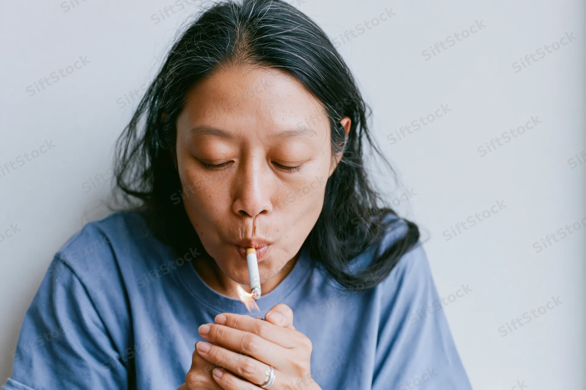 Asian woman lighting a cigarette held between her lips indoors