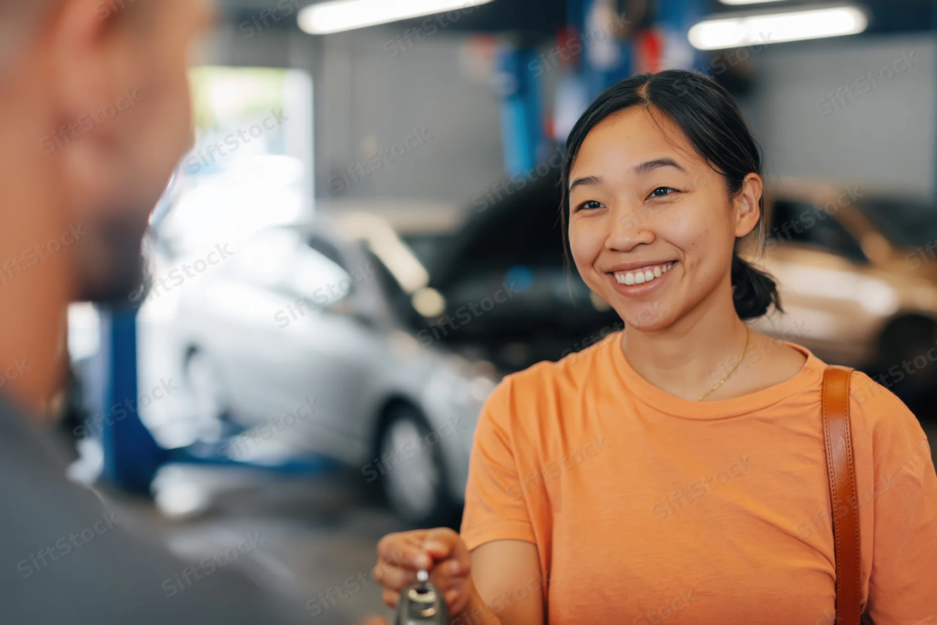 Young asian woman smiling while receiving car keys from mechanic in garage