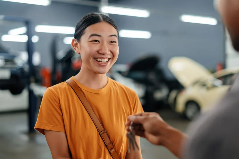 Young asian woman smiling as she receives car keys from mechanic in auto repair garage