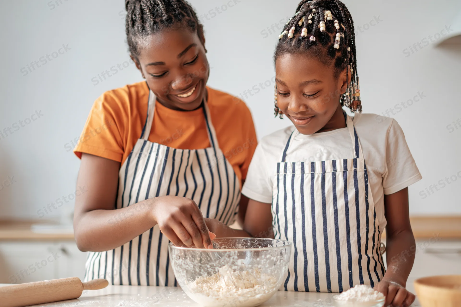 Mother and daughter baking together in kitchen wearing striped aprons