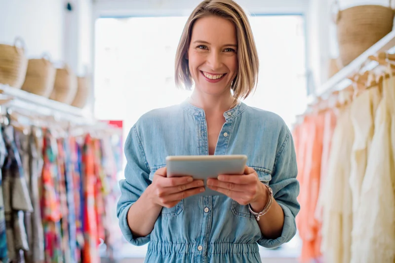 Smiling woman holding tablet in boutique clothing store