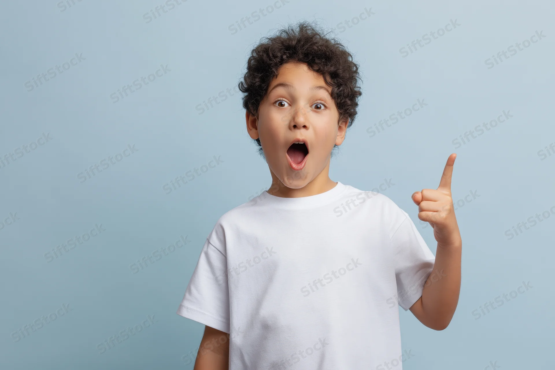 Young boy with curly dark hair pointing upward with surprised expression in studio setting