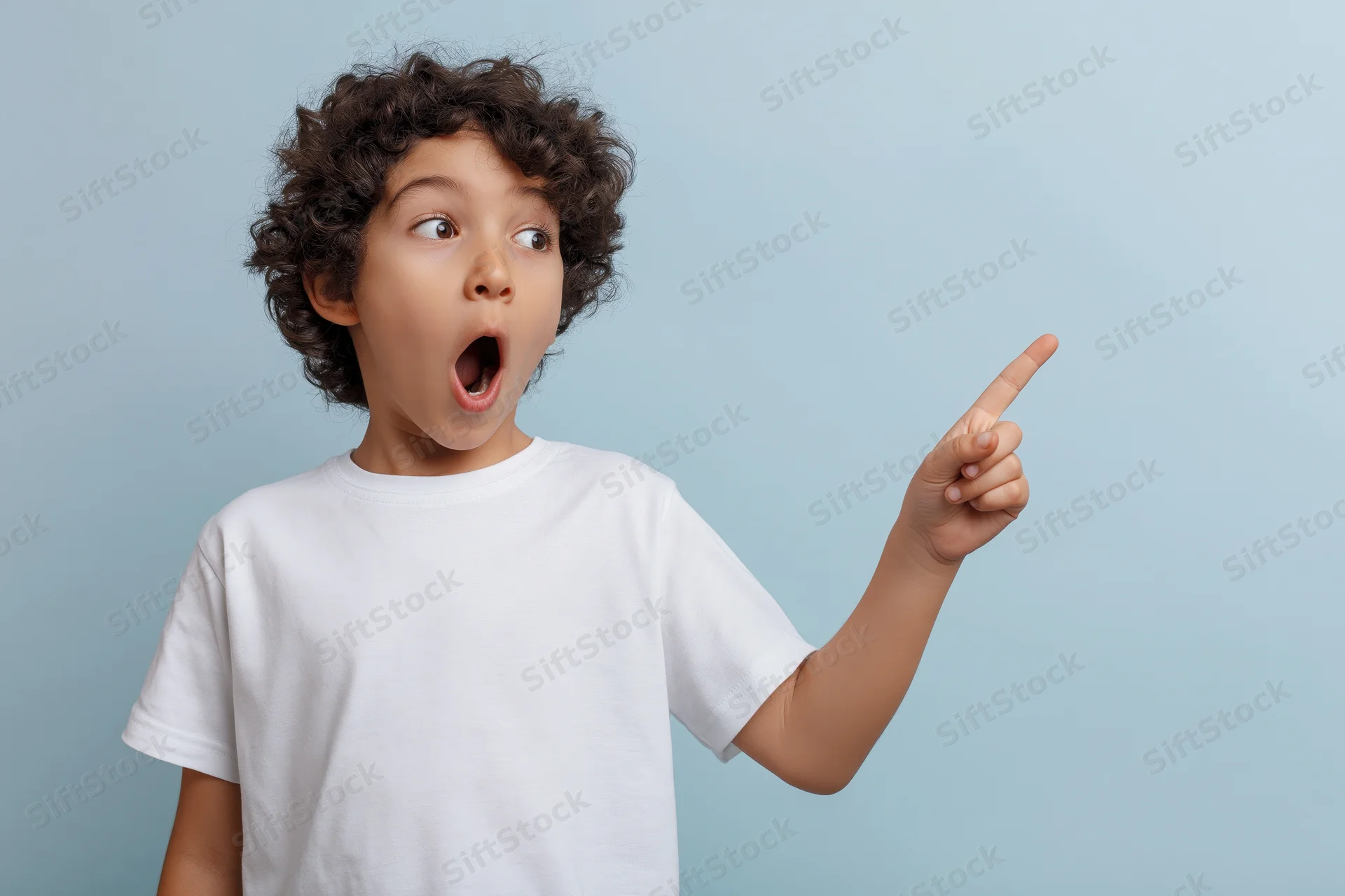 Young boy with curly dark hair pointing upward in surprise against a light blue background