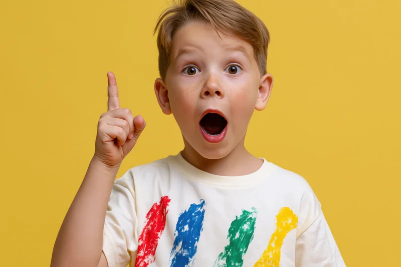 Young boy with wide eyes and open mouth pointing upward in excited expression against yellow background