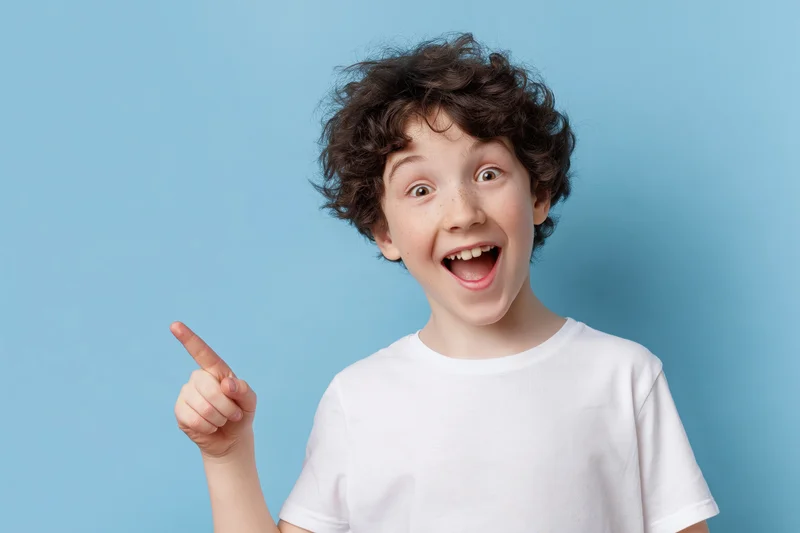 Young boy with curly dark brown hair pointing excitedly against blue background