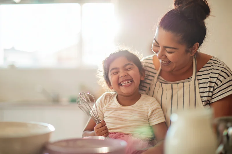 Mother and daughter laughing while baking together in the kitchen