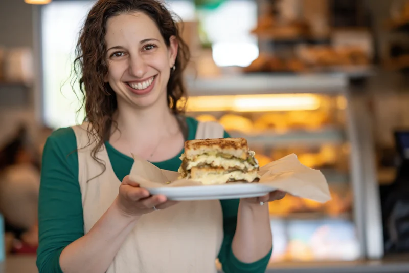 Woman holding a grilled cheese sandwich on a plate in a cafe