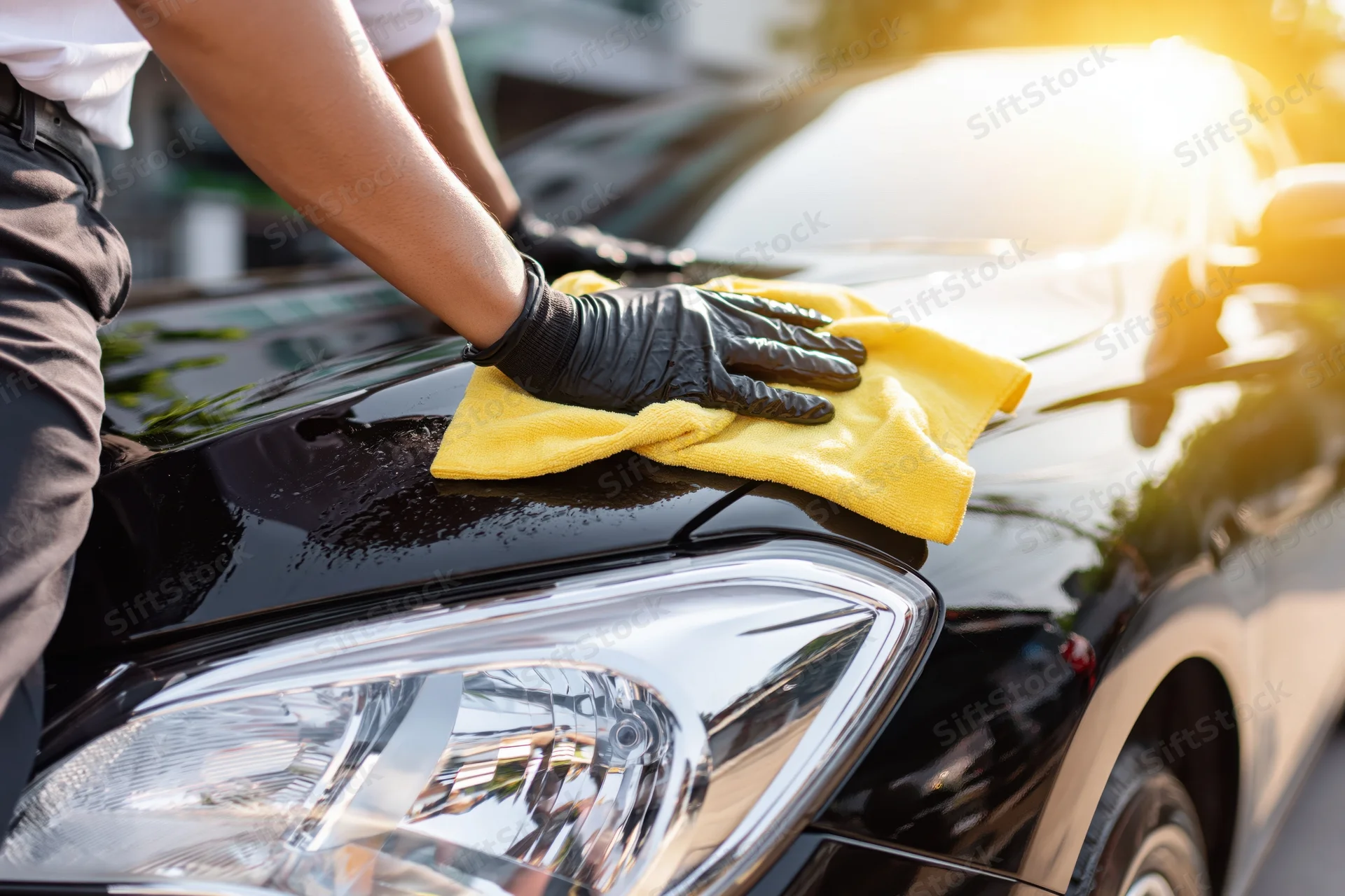Man polishing black car hood with yellow cloth outdoors