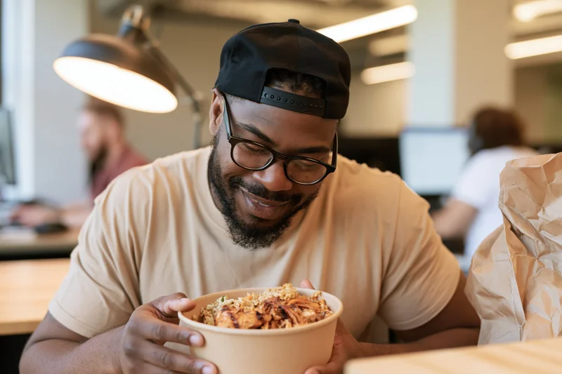 Man eating takeout lunch from a bowl at his office desk