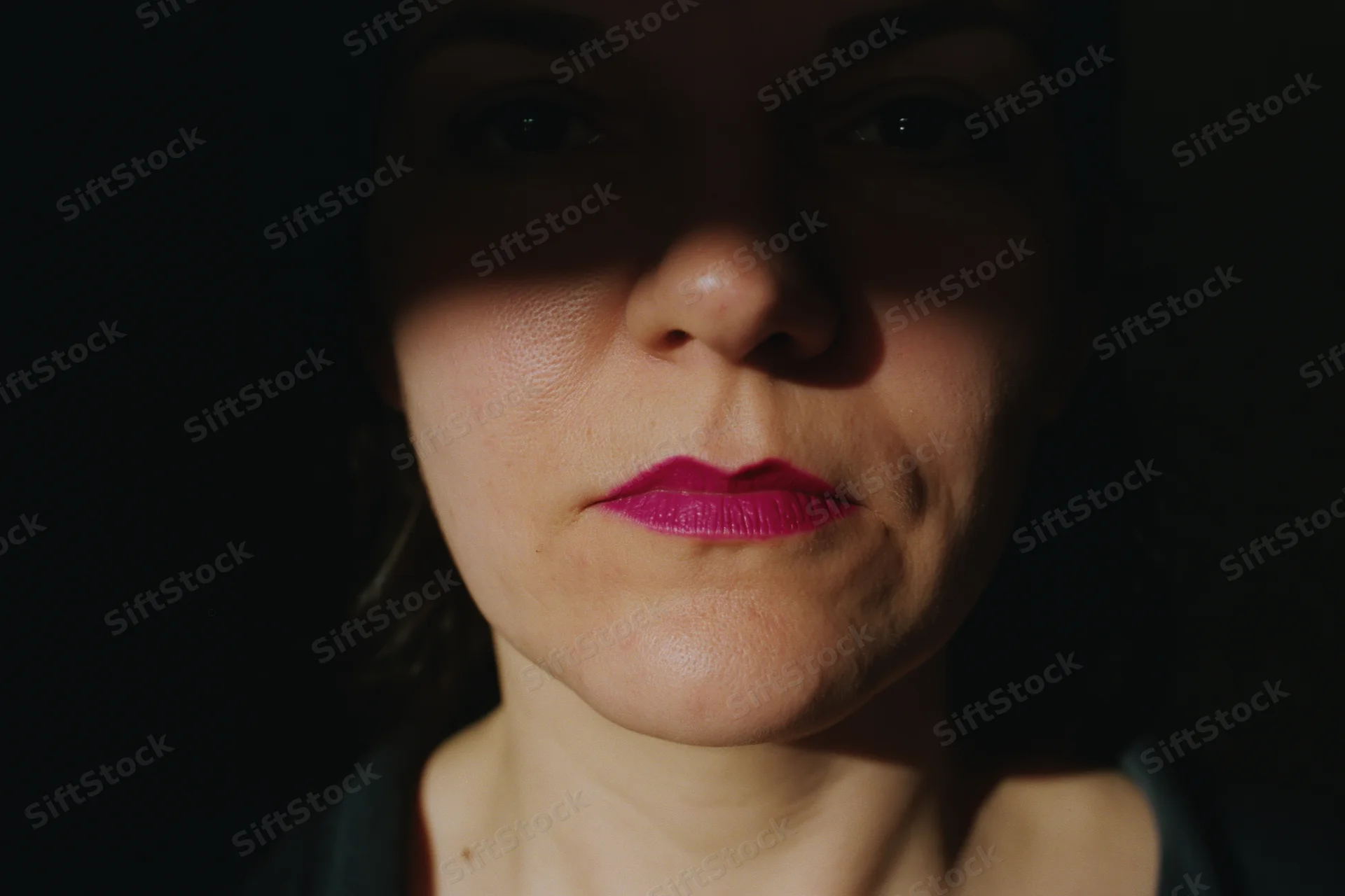 Closeup portrait of a woman with pink lipstick and dramatic shadow lighting