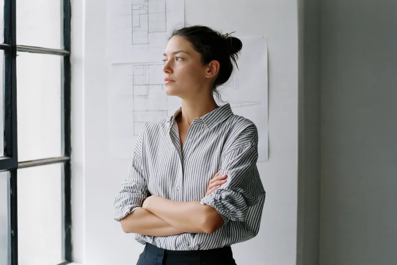 Woman architect standing by window with arms crossed in office studio