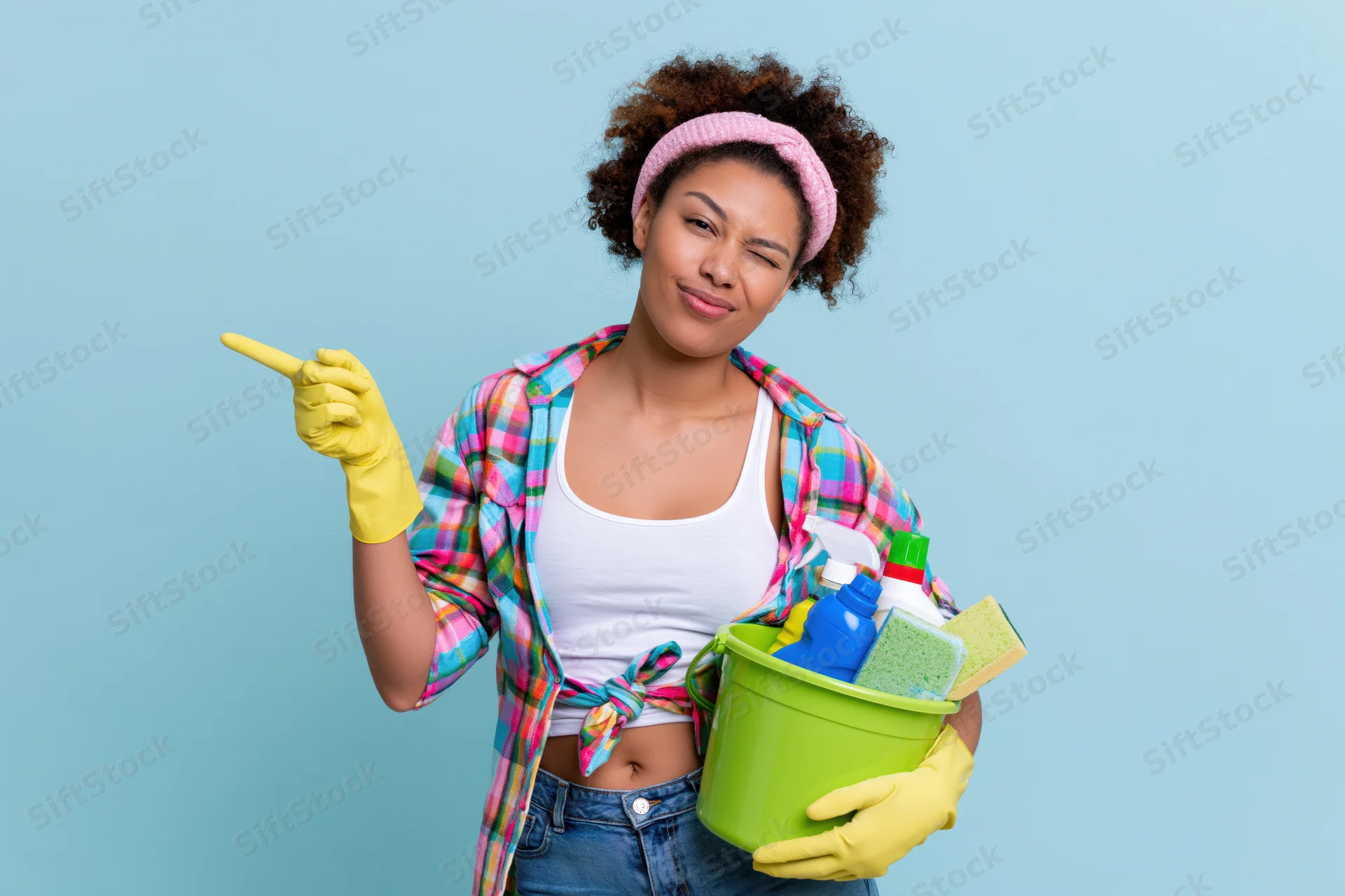 Woman winking and pointing while holding a green bucket of cleaning supplies against a blue background