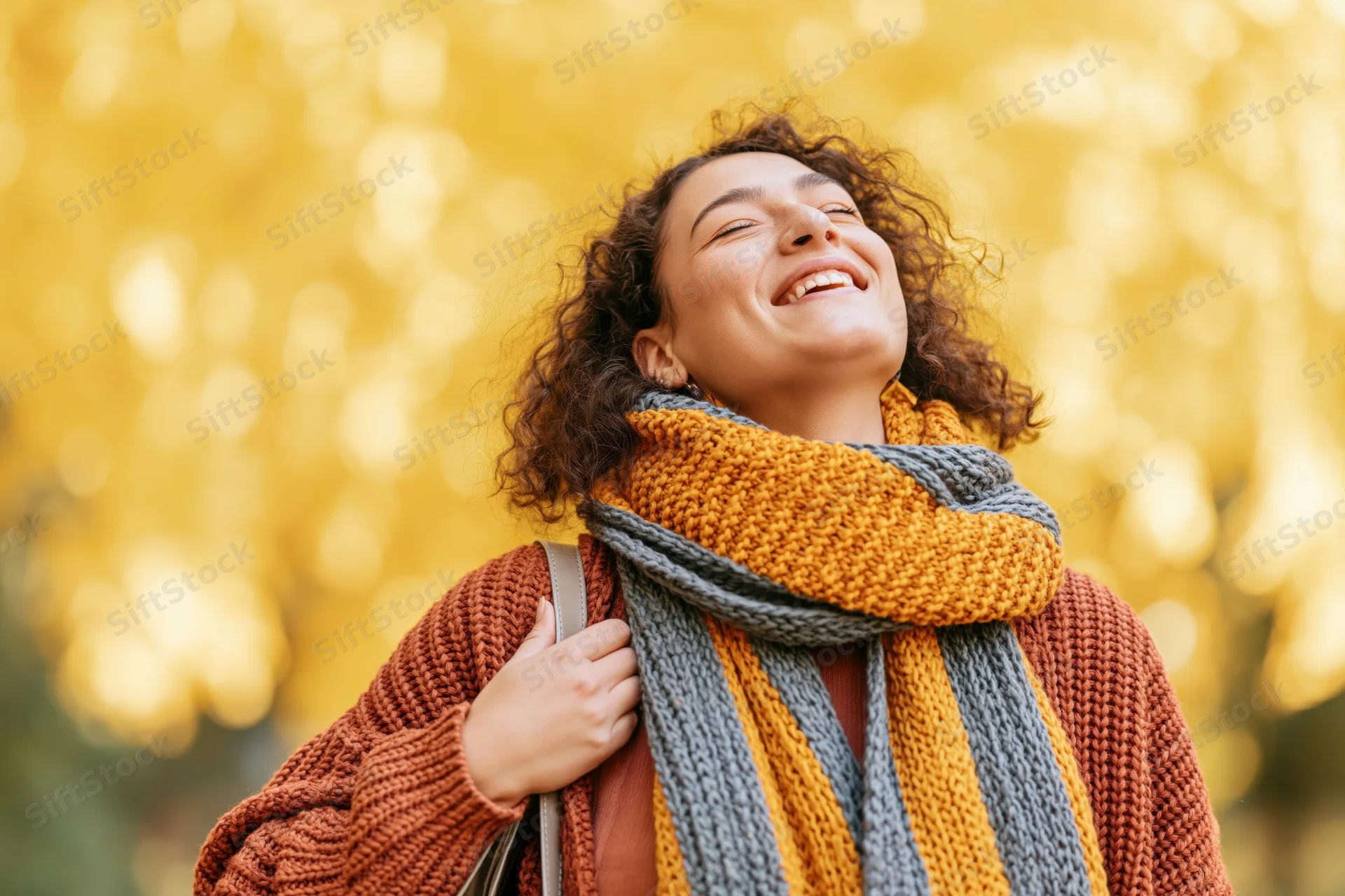 Young woman laughing joyfully outdoors in autumn with yellow foliage behind her