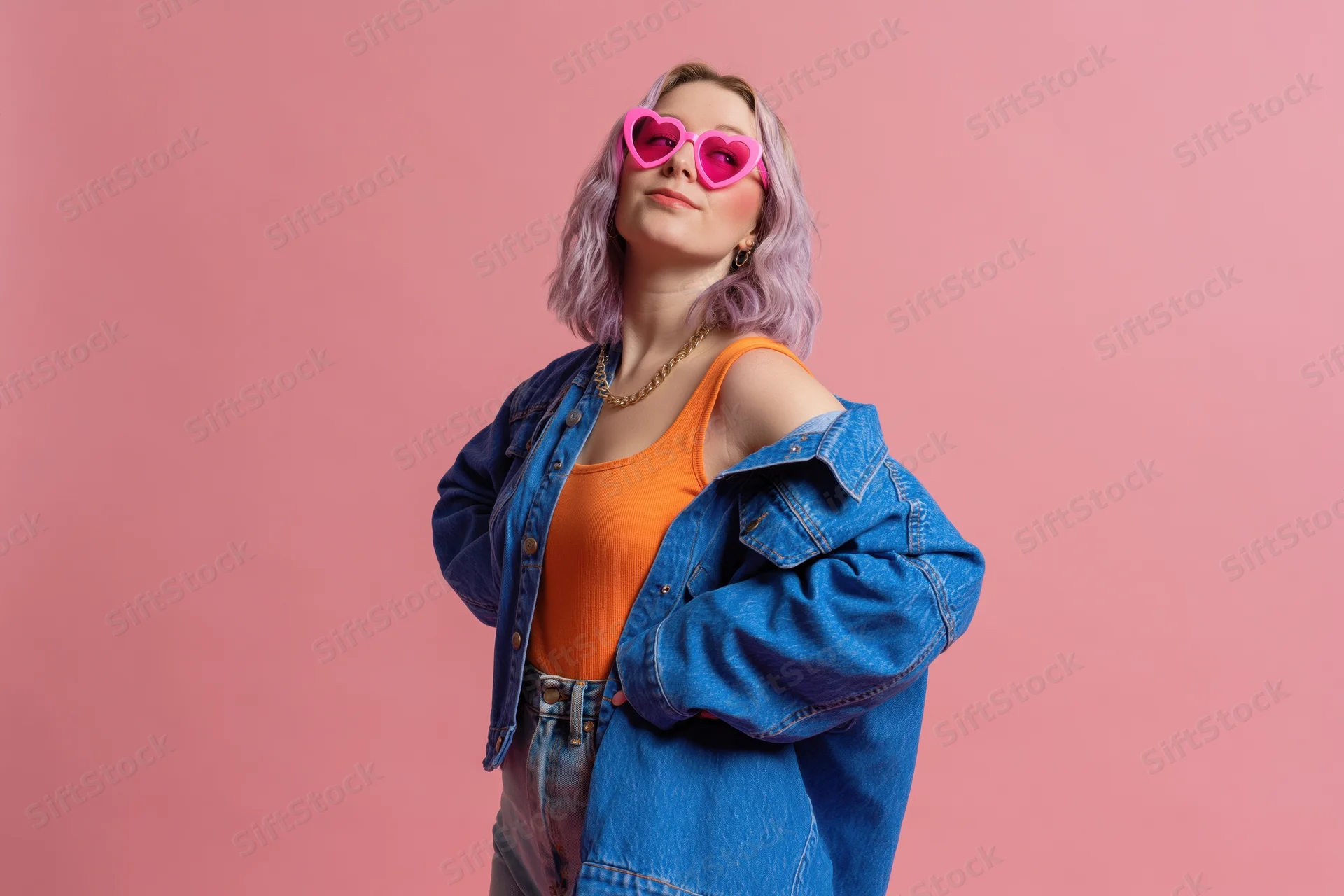 Young woman with lavender hair wearing heart-shaped pink sunglasses and denim jacket posing against pink background