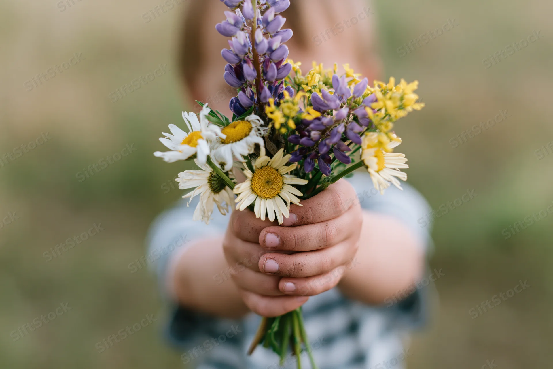 Child holding out a wildflower bouquet toward the camera in a field