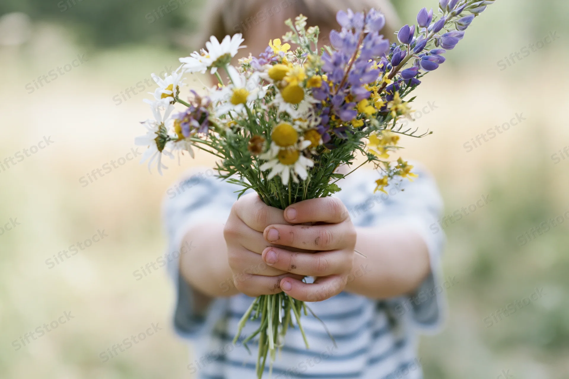 Child holding wildflower bouquet toward camera in outdoor setting
