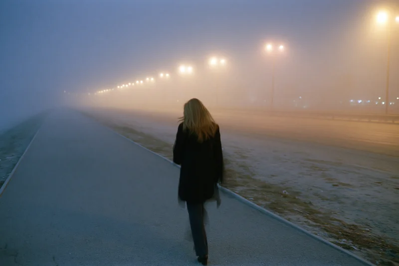 Woman walking alone on a foggy city sidewalk at night