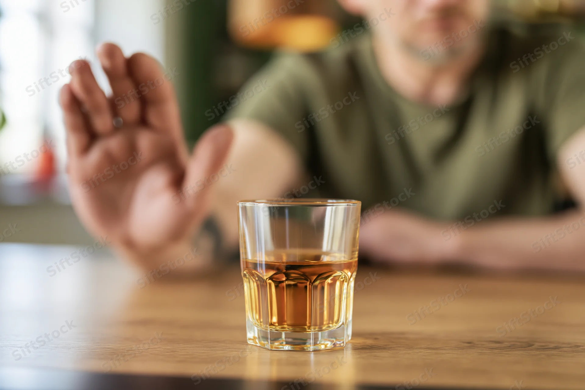 Man extending open hand to refuse whiskey glass on wooden bar table