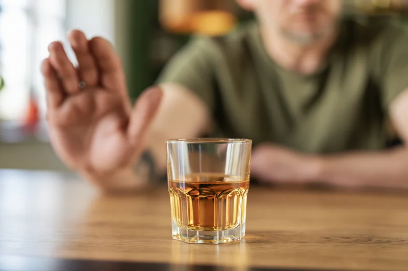 Man extending open hand to refuse whiskey glass on wooden bar table