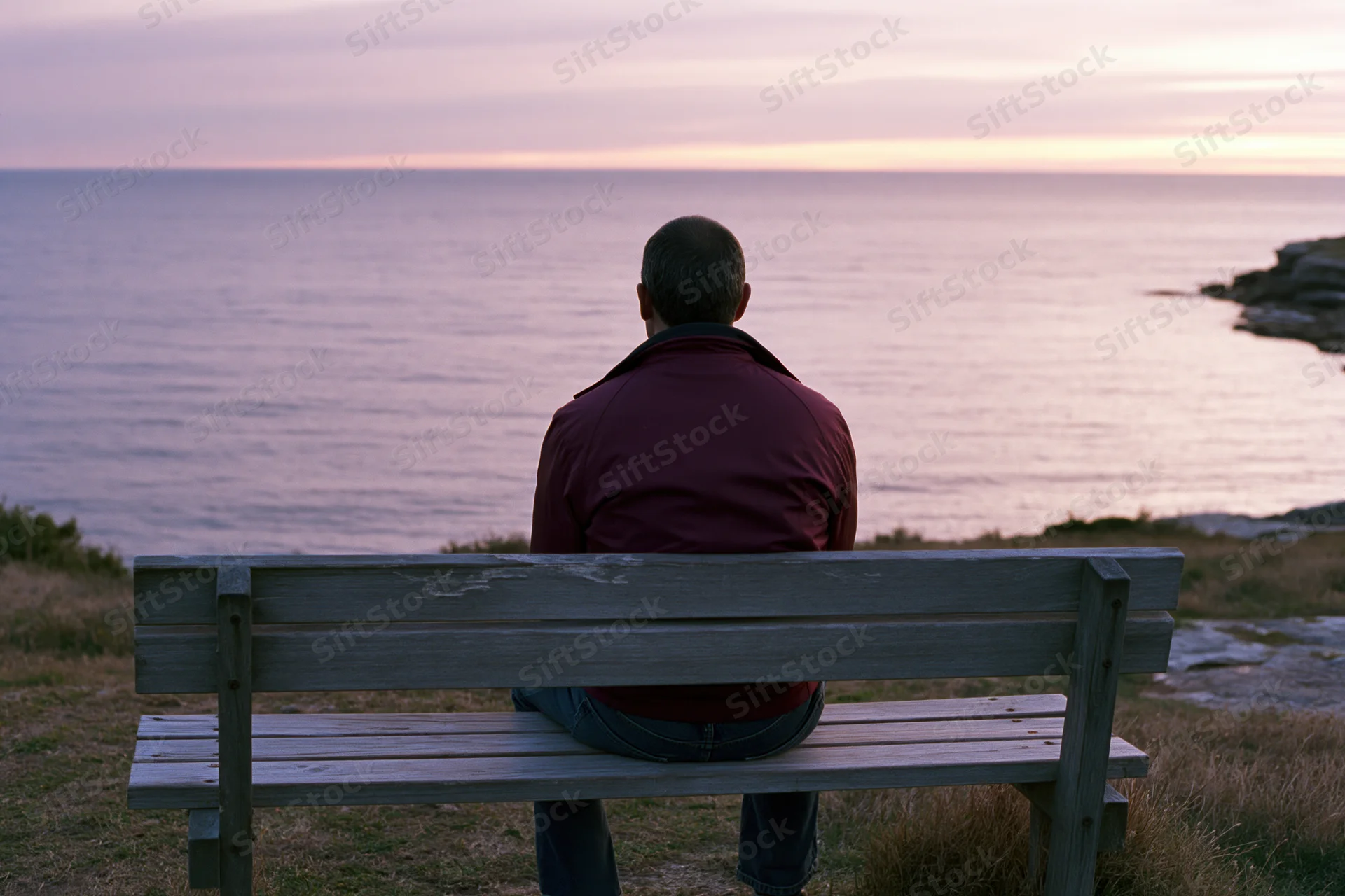 Man sitting alone on wooden bench facing ocean at sunset