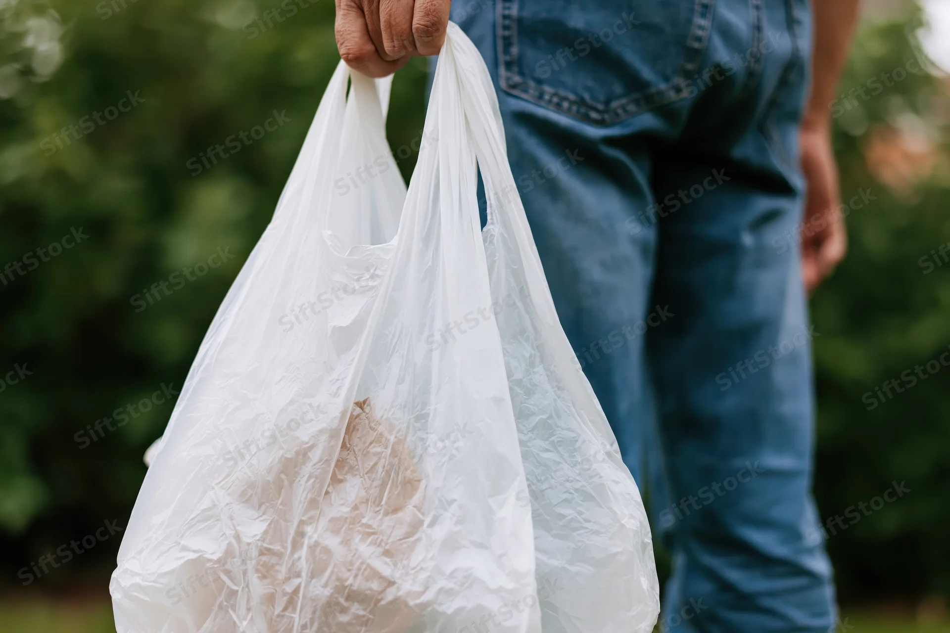 Person holding white plastic shopping bags outdoors in hand