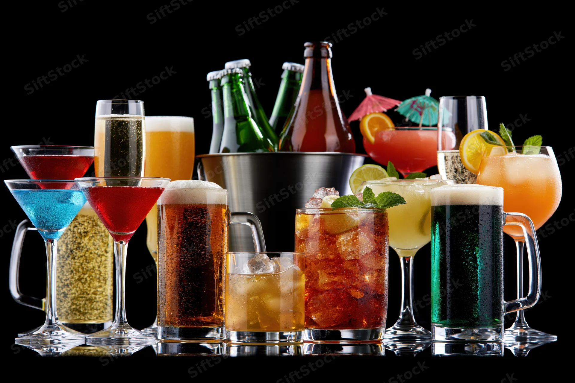 Assorted alcoholic drinks arranged in a row on a reflective surface against black background