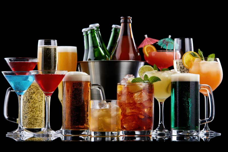 Assorted alcoholic drinks arranged in a row on a reflective surface against black background