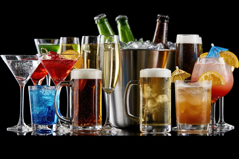 Assorted alcoholic drinks in various glasses and bottles arranged in a row on a reflective surface