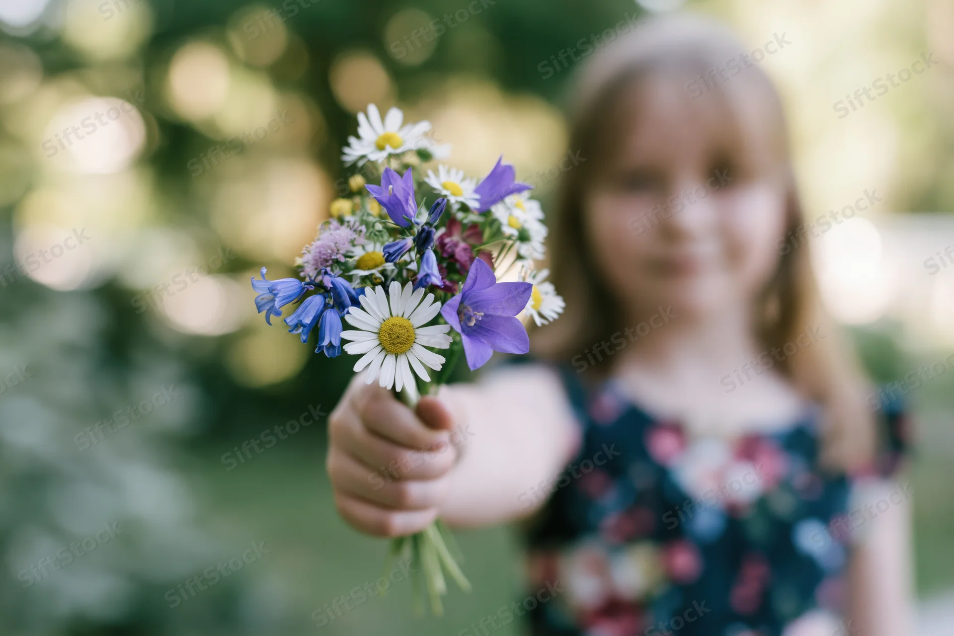 Young girl extending a small wildflower bouquet toward the camera in a sunlit garden
