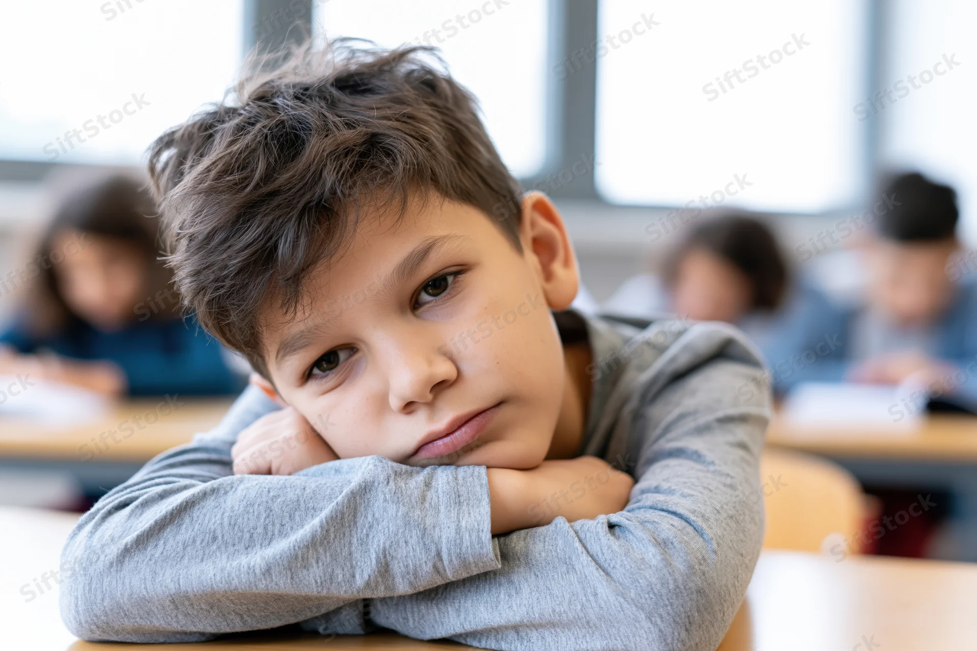 Young boy resting his head on folded arms at a desk in a classroom