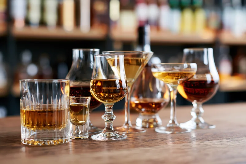 Various glasses filled with amber-colored spirits arranged on a wooden bar counter