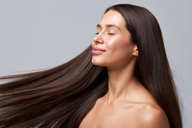 Young woman with long glossy dark hair in side profile, eyes closed and smiling, in studio setting
