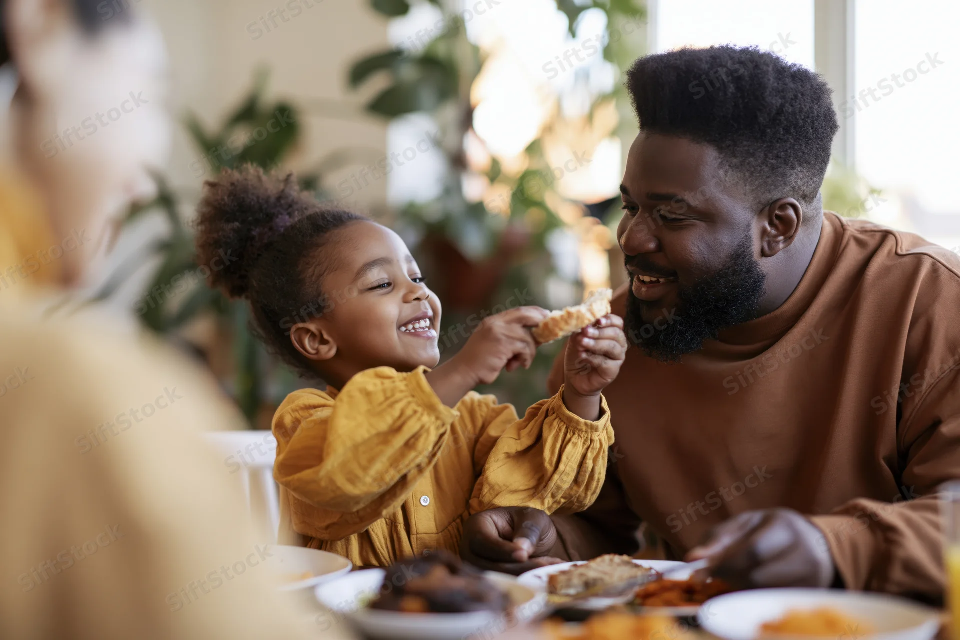 Black father and young daughter sharing a slice of bread at dining table