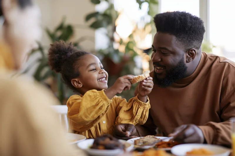 Black father and young daughter sharing a slice of bread at dining table